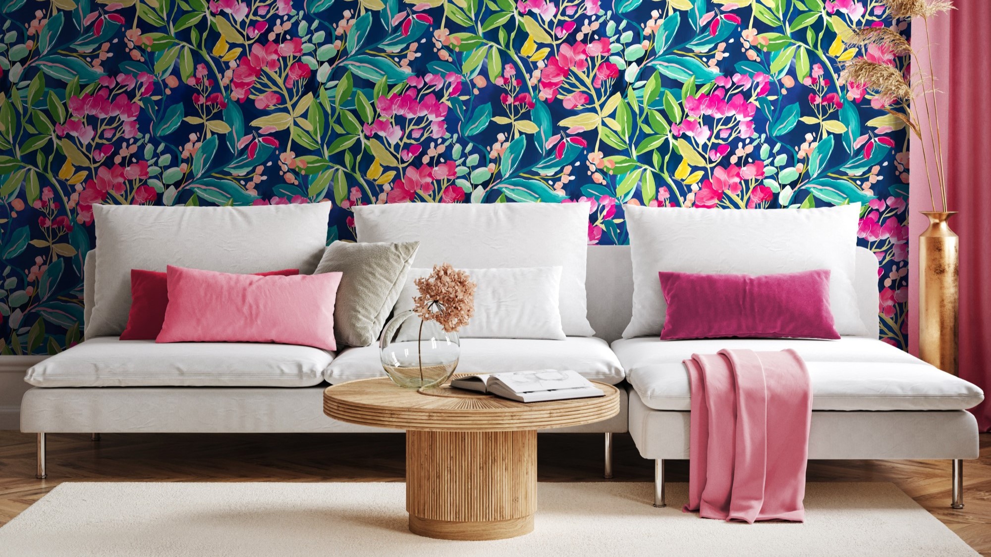 Living room with colourful floral wallpaper on one wall and a pink couch with a round coffee table in front of it. There is a white lamp on the coffee table and a green plant behind the couch.