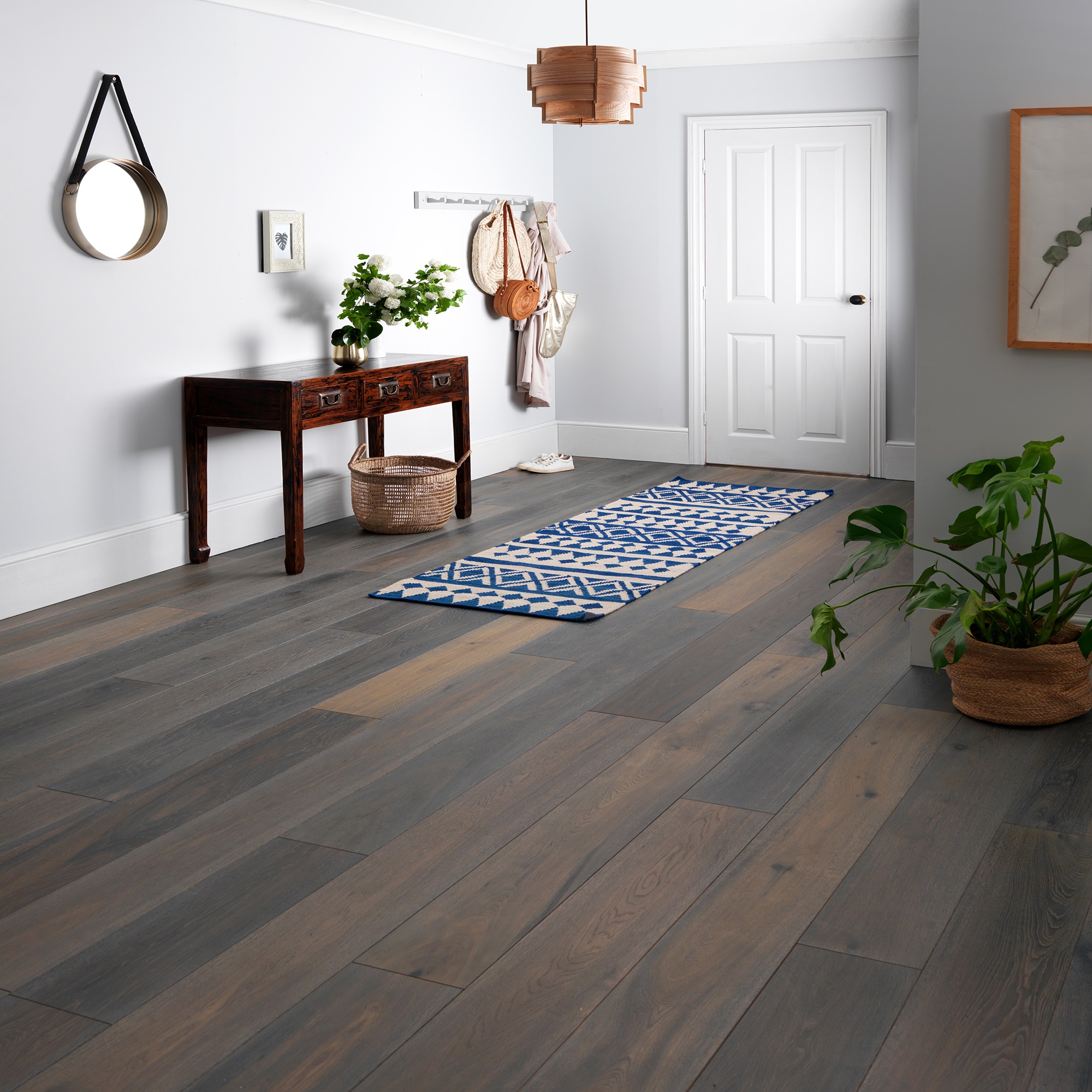 A long hallway with a light wooden floor and a brown wooden table in the centre. The table has a small potted plant and a decorative bowl on top.