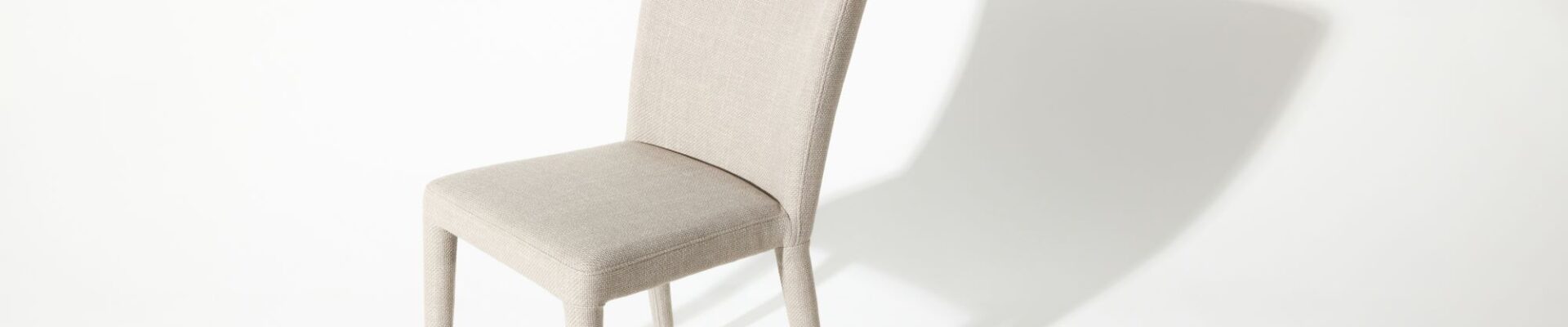 A modern white chair with a simple design casts a shadow on a white background