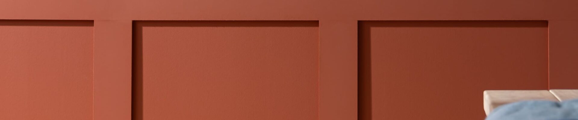 A red wooden panelled wall with a simple, light coloured wooden table in front of it.