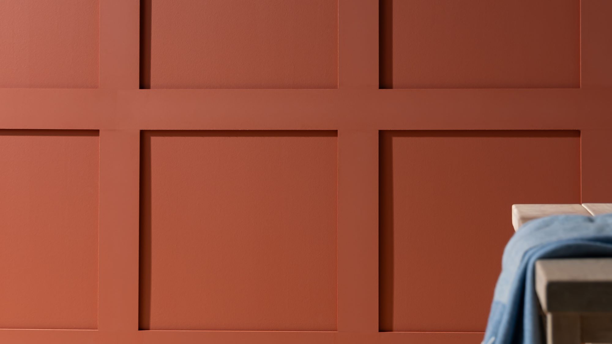 A red wooden panelled wall with a simple, light coloured wooden table in front of it.