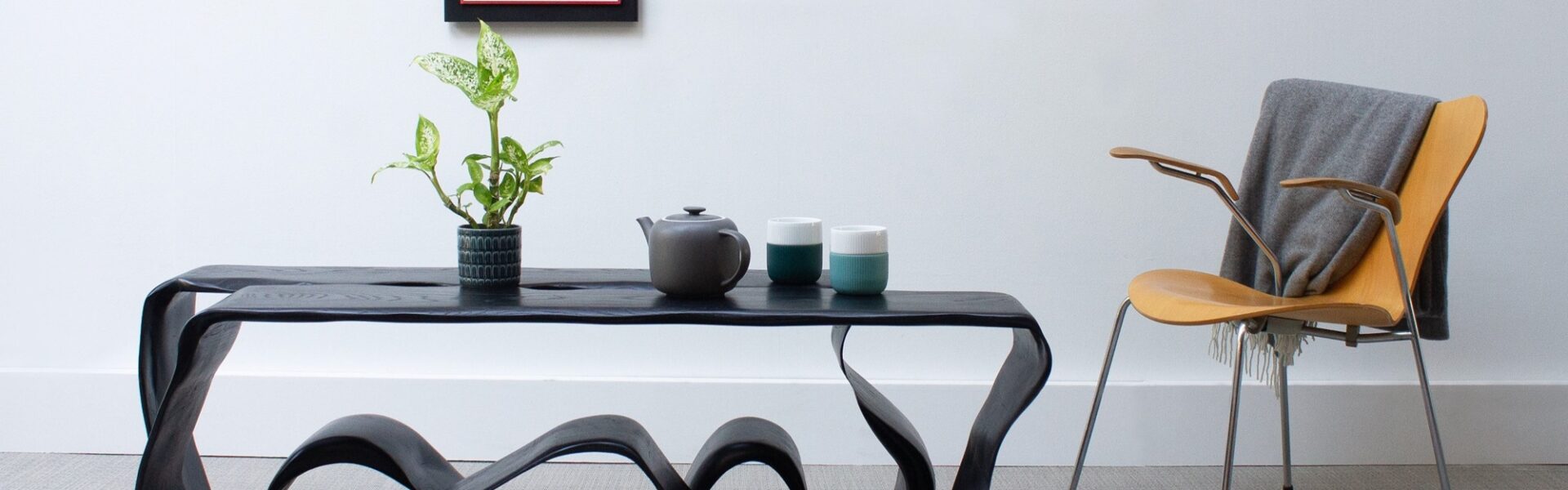 A coffee table with distinctive feet and chair in a living room with an orange image on the wall.