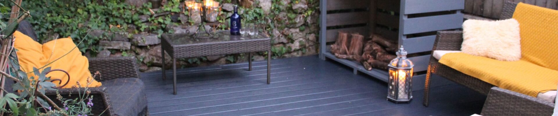A relaxing outdoor space featuring a dark wicker furniture set and a fire pit. The wicker furniture includes two chairs, a loveseat, and a small table. The fire pit is made of black metal.