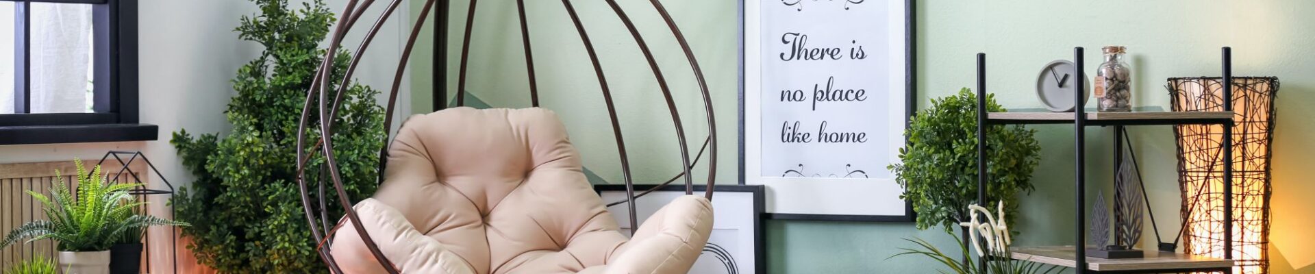 A cosy living room in sage green with a hanging chair in the corner. The chair is made of woven rope and has a cream-coloured cushion. There is a small side table next to the chair with a cup of coffee and a book on it.