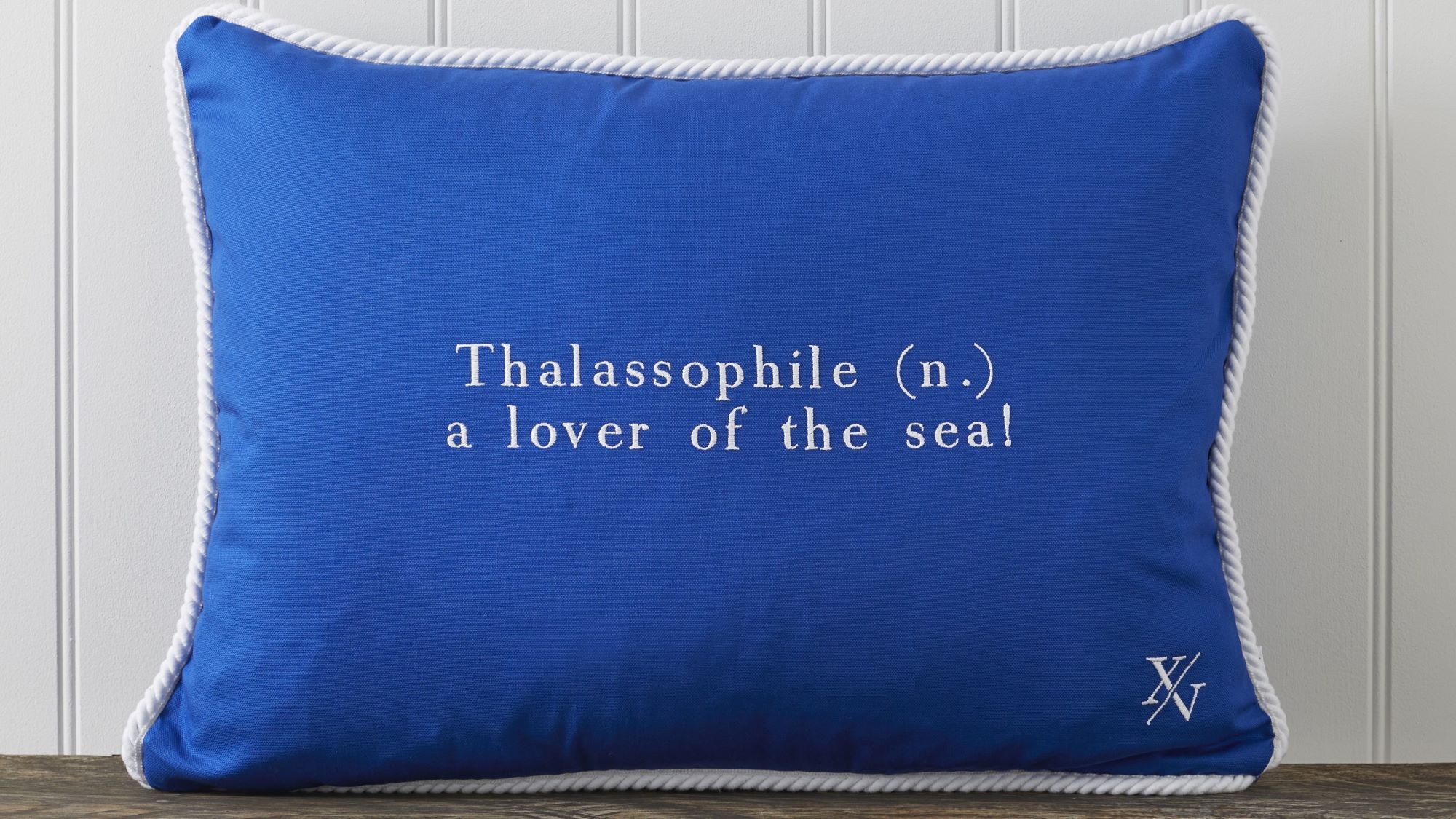 Cushion featuring the word "Thalassophile" embroidered on it in white. The word "Thalassophile" means "a lover of the sea". The cushion also has a white rope trim around the edges.