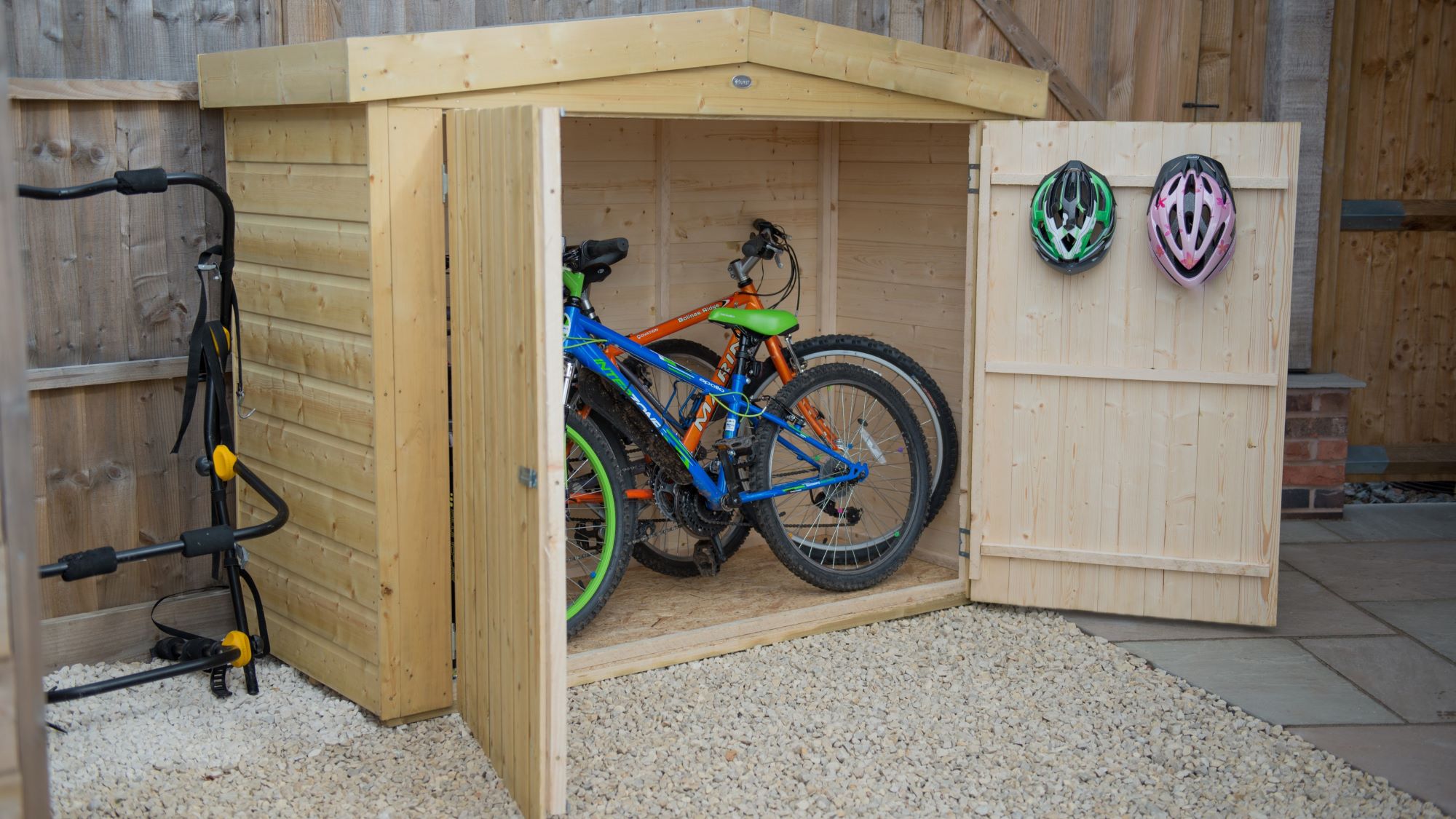 Wooden bike shed with double doors open, revealing two bicycles inside.