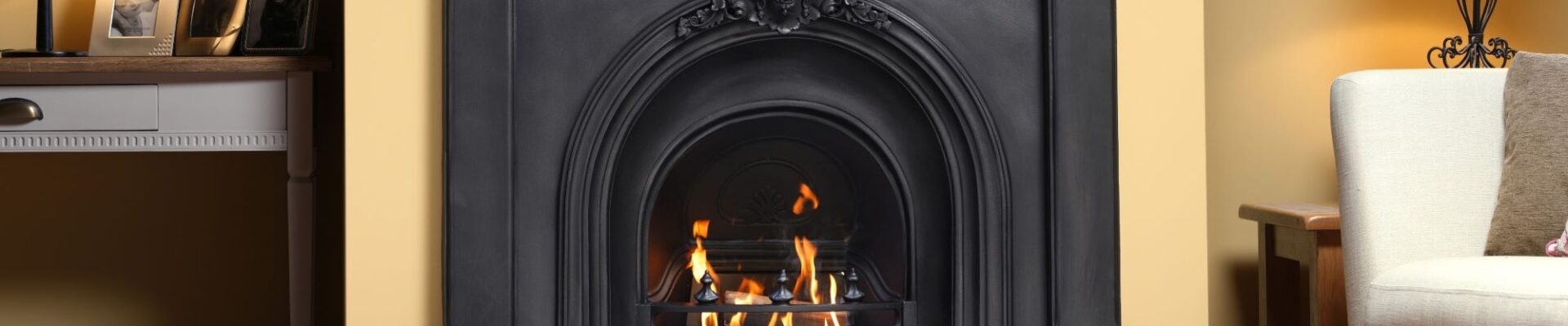 Black cast iron fireplace with a glowing gas fire, set in a traditional living room with a cream wall.