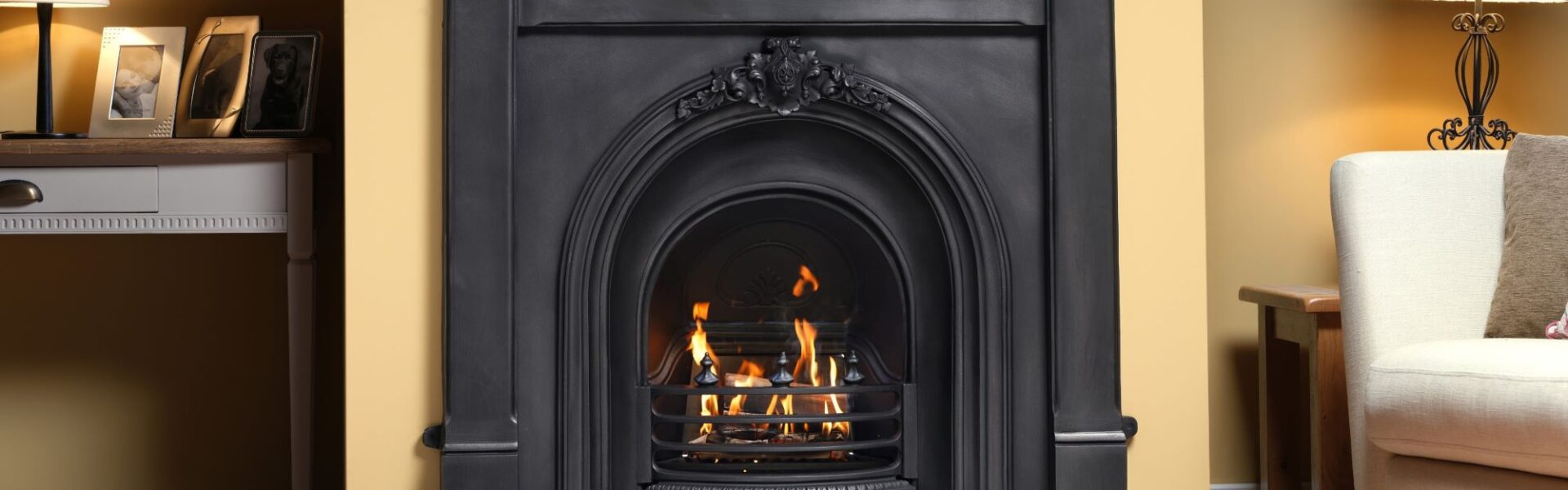Black cast iron fireplace with a glowing gas fire, set in a traditional living room with a cream wall.