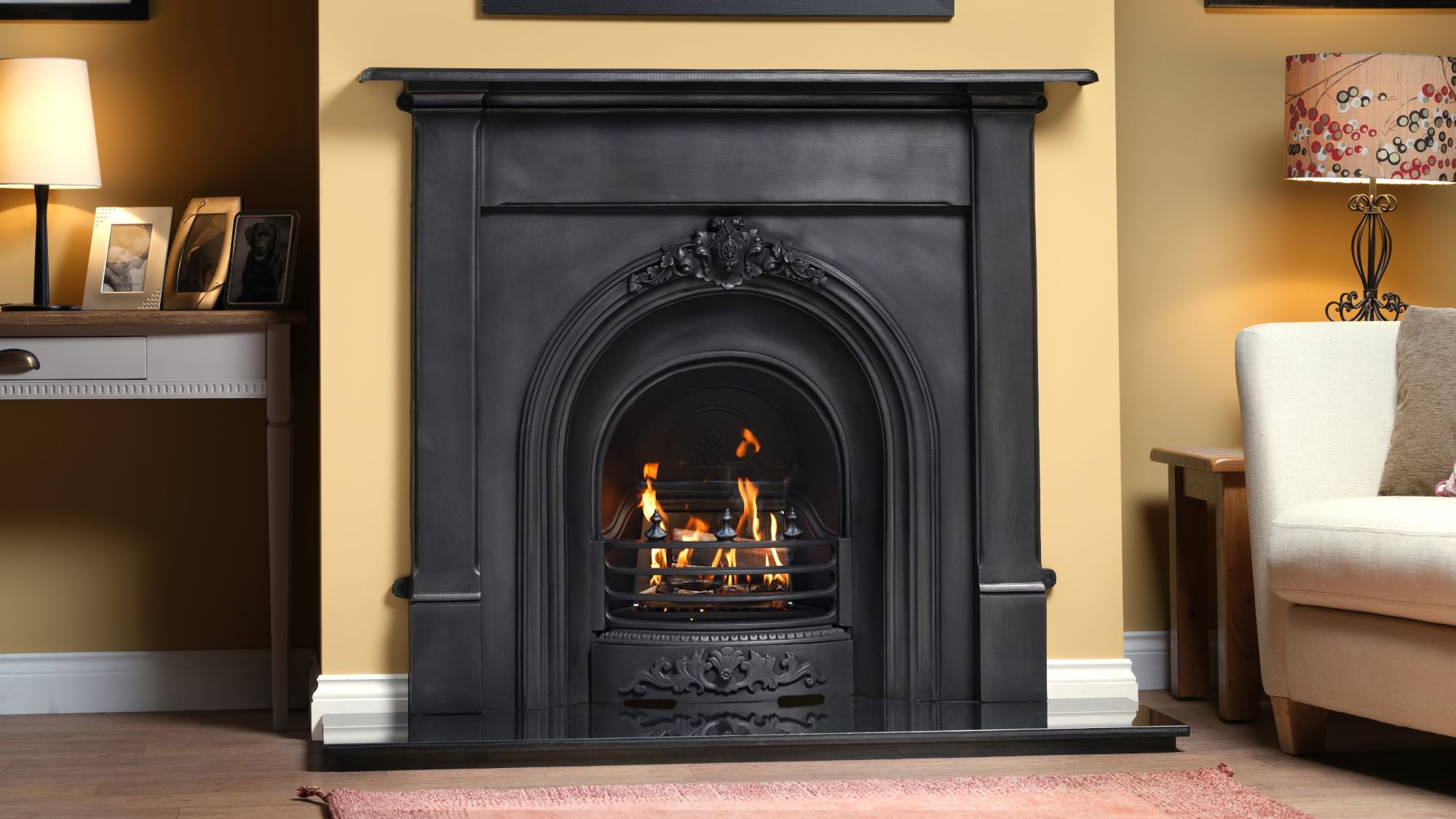 Black cast iron fireplace with a glowing gas fire, set in a traditional living room with a cream wall.