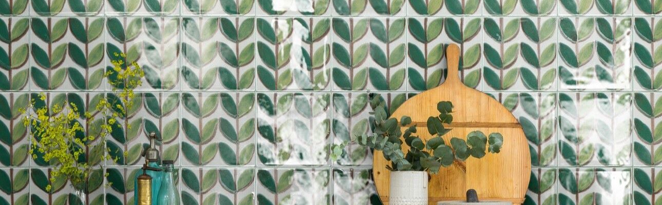 A green and white patterned tile splashback. The tiles feature a leaf-like design and are arranged in a grid pattern. The overall style of the kitchen is vintage and retro, with a focus on natural materials and warm colours.