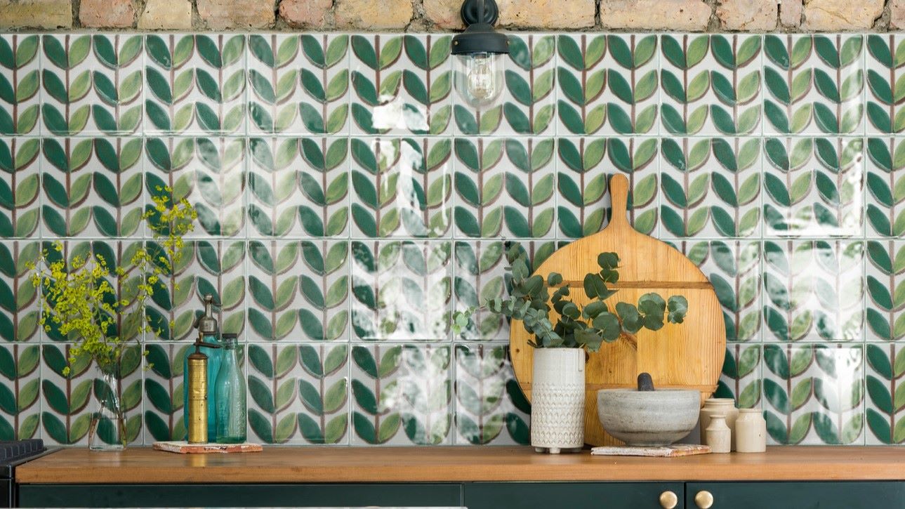 A green and white patterned tile splashback. The tiles feature a leaf-like design and are arranged in a grid pattern. The overall style of the kitchen is vintage and retro, with a focus on natural materials and warm colours.