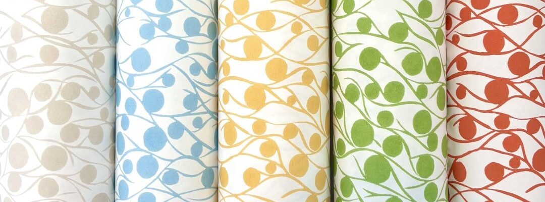 Five rolls of fabric with a repeating pattern of circles and lines. The circles are different colours on each roll: cloud, blue, yellow, green, and coral. The lines are white on each roll and create a wavy pattern that connects the circles.