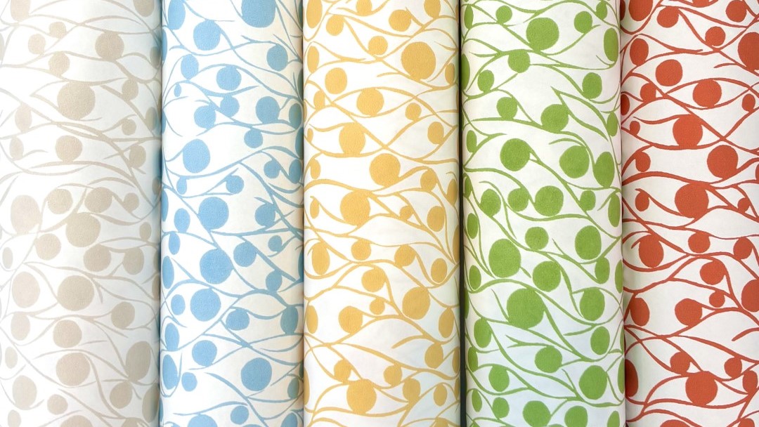 Five rolls of fabric with a repeating pattern of circles and lines. The circles are different colours on each roll: cloud, blue, yellow, green, and coral. The lines are white on each roll and create a wavy pattern that connects the circles.