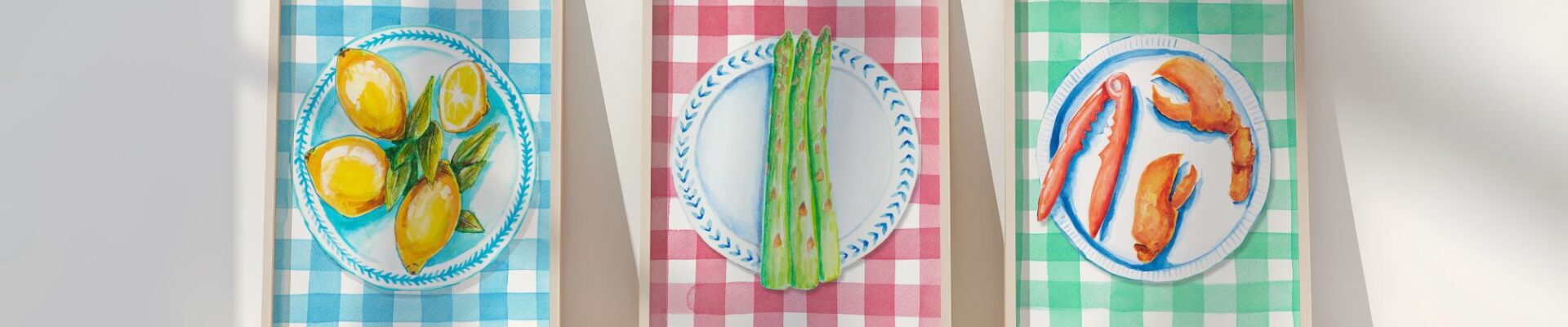 Three framed illustrations of food on plates. The left image shows lemons on a blue and white plate against a blue and white gingham background. The middle image shows asparagus on a blue and white plate against a red and white gingham background. The right image shows lobster claws on a blue and white plate against a green and white gingham background.