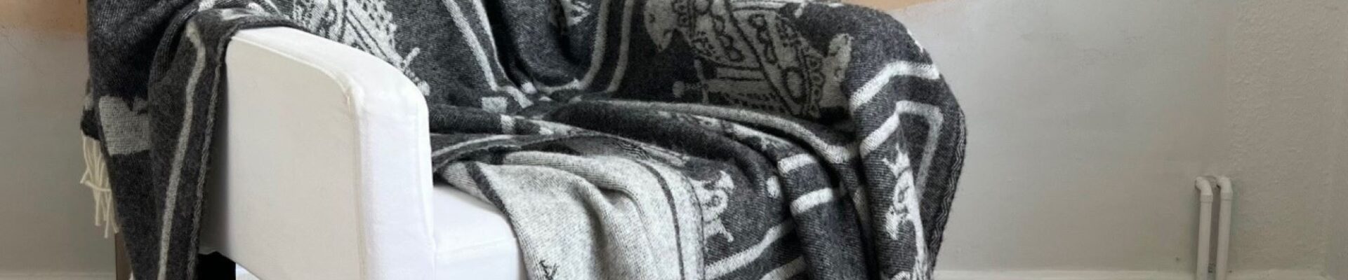 A cosy grey throw blanket with a playing card pattern draped over a white armchair.