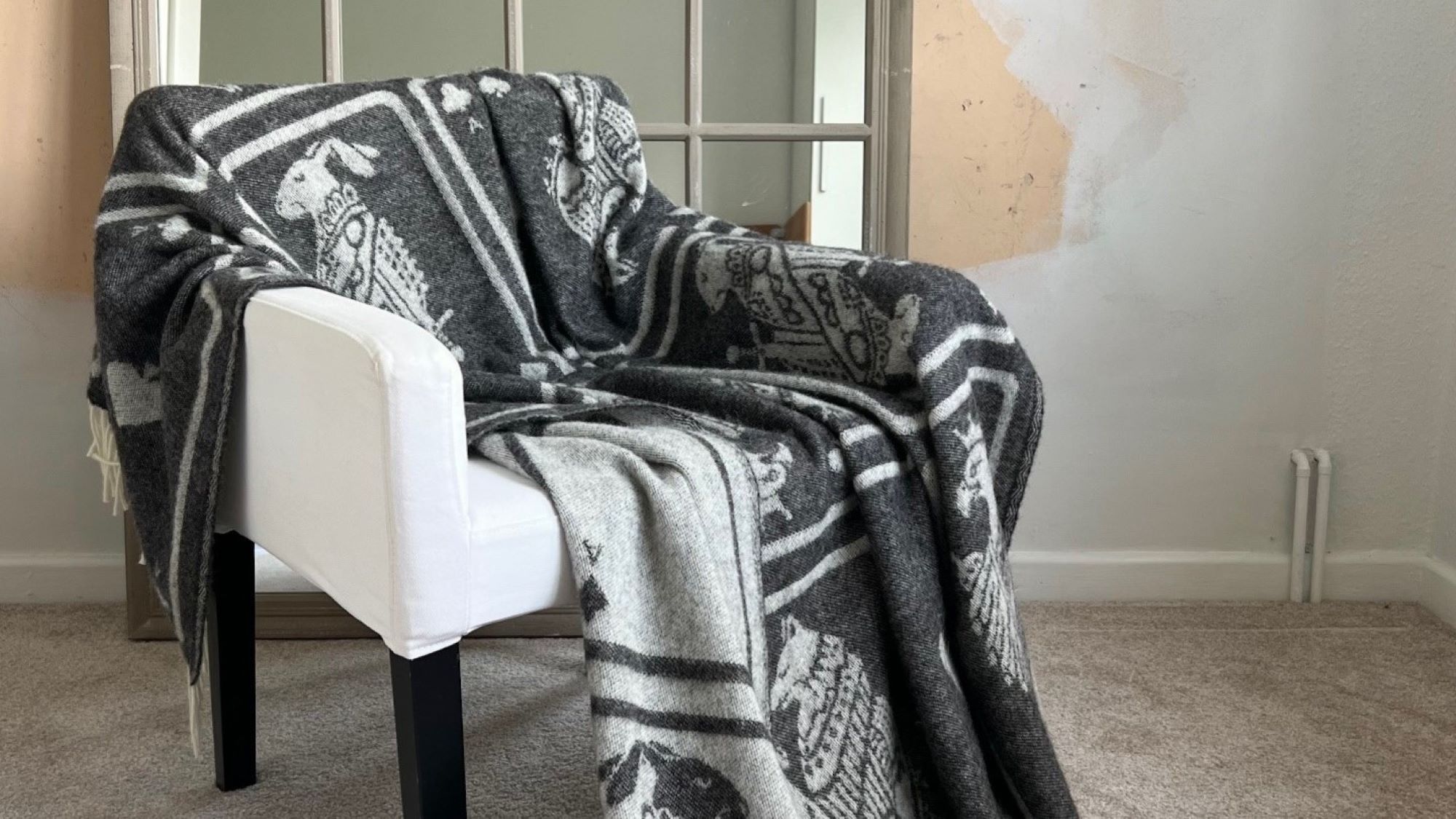 A cosy grey throw blanket with a playing card pattern draped over a white armchair.