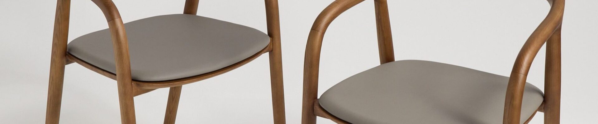 A pair of contemporary wooden dining chairs with curved backs and grey upholstered seats.