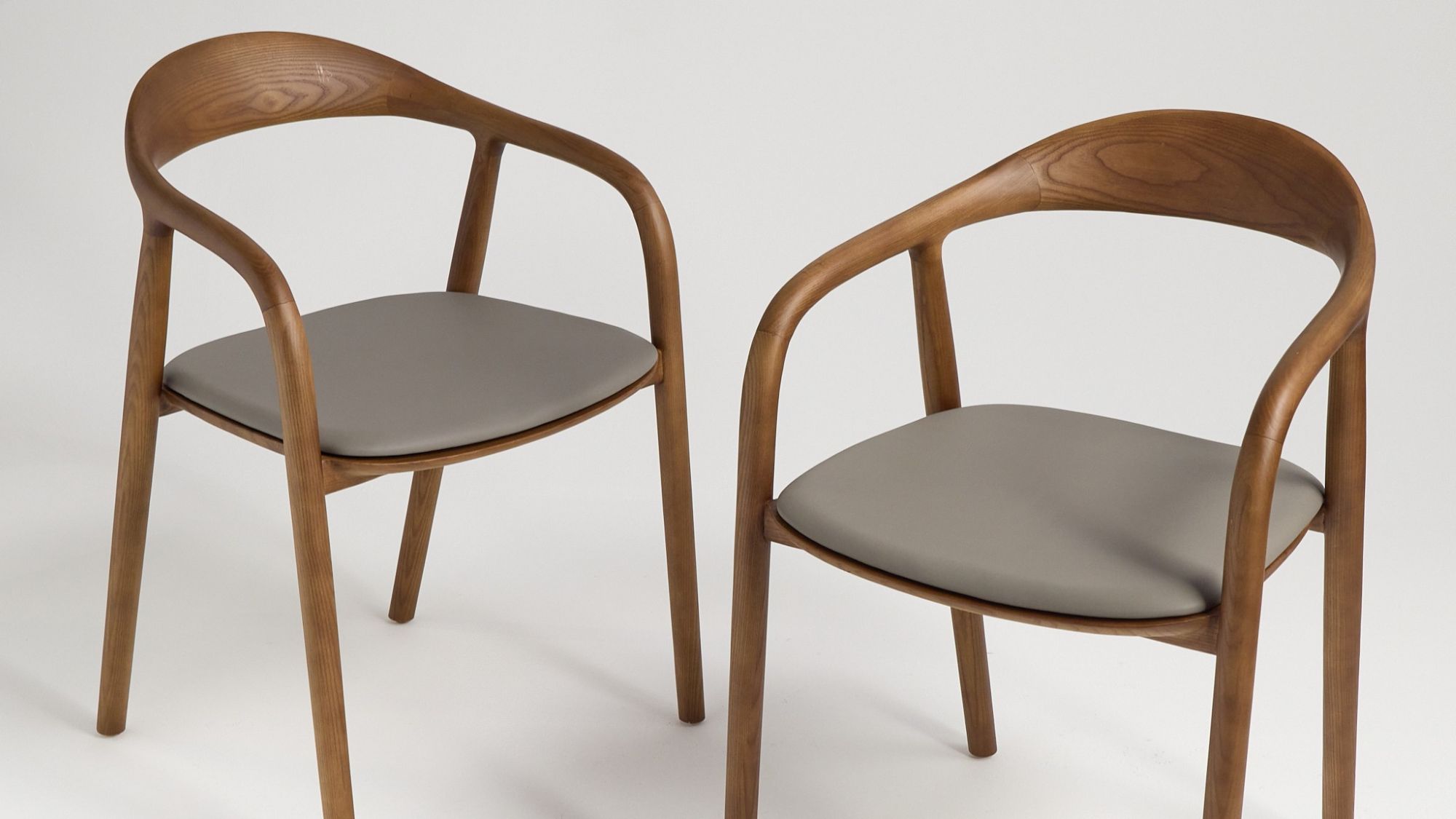 A pair of contemporary wooden dining chairs with curved backs and grey upholstered seats.