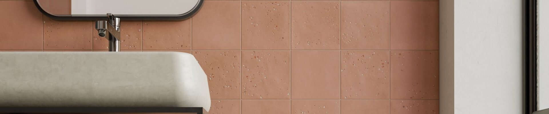 A bathroom wall tiled with square, textured terracotta tiles in a grid pattern. A white sink and black framed mirror are partially visible.