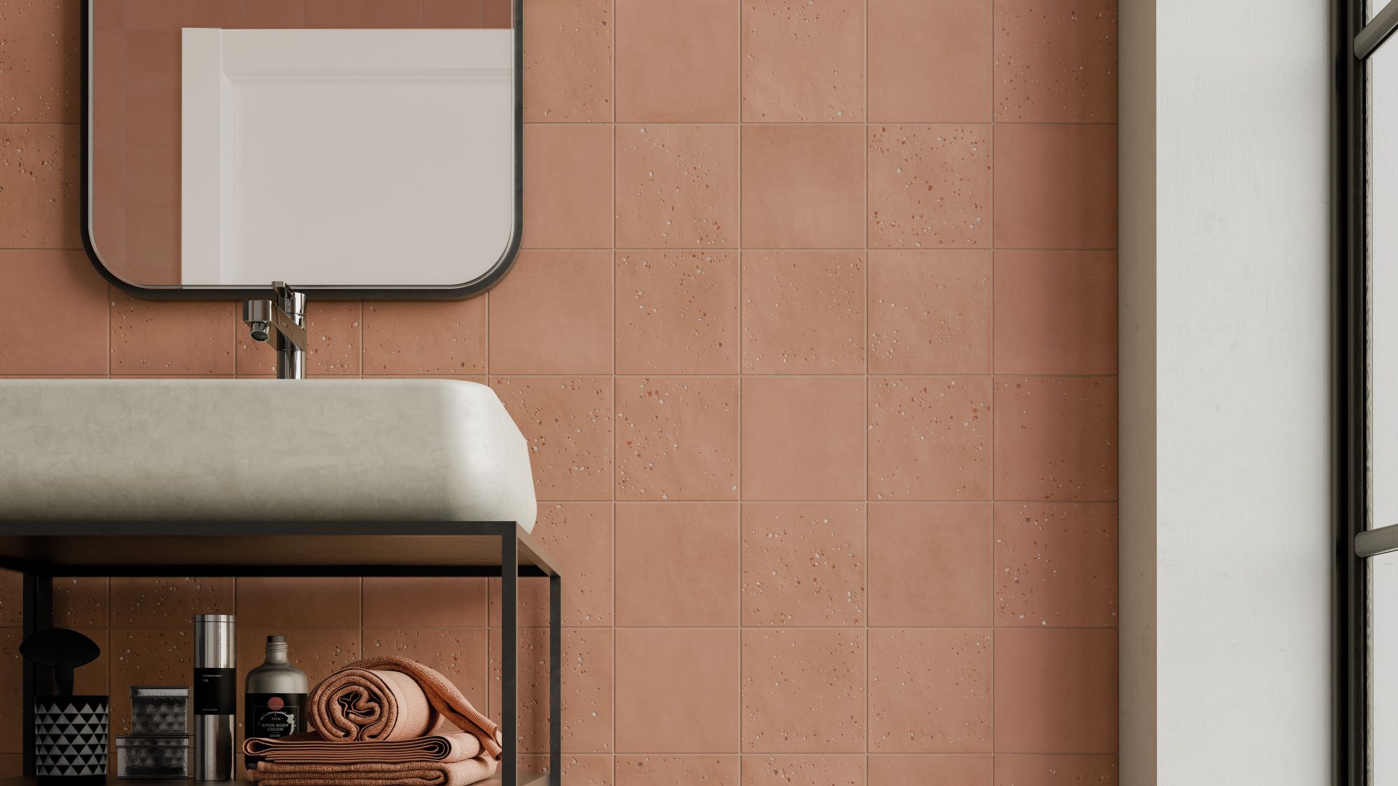 A bathroom wall tiled with square, textured terracotta tiles in a grid pattern. A white sink and black framed mirror are partially visible.