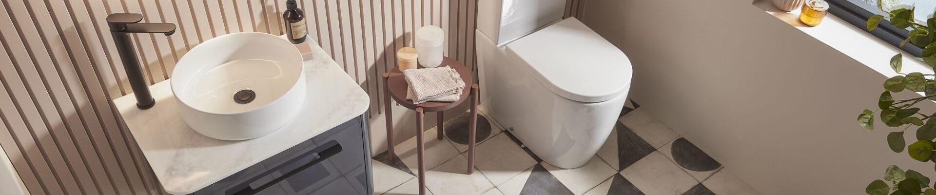 An overhead shot of a modern bathroom with a white vessel sink on a dark grey vanity, a white toilet, and patterned geometric floor tiles.