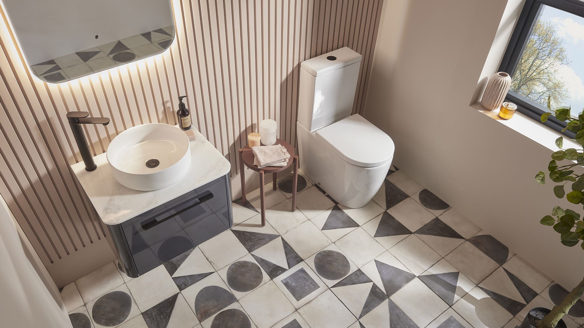An overhead shot of a modern bathroom with a white vessel sink on a dark grey vanity, a white toilet, and patterned geometric floor tiles.