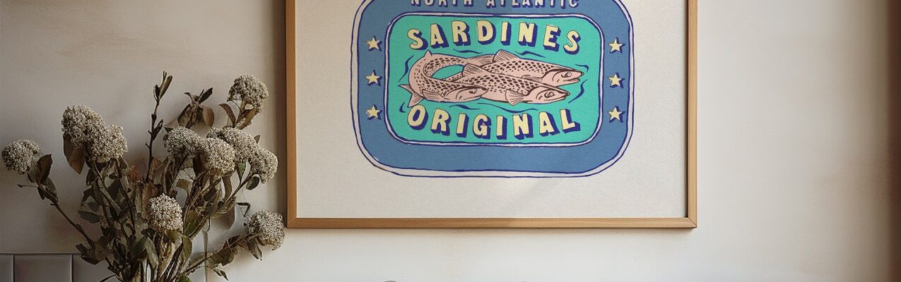 A framed illustration of a vintage sardine can label hangs on a white wall above a kitchen counter. The label features three sardines swimming in a blue oval surrounded by a light blue border.