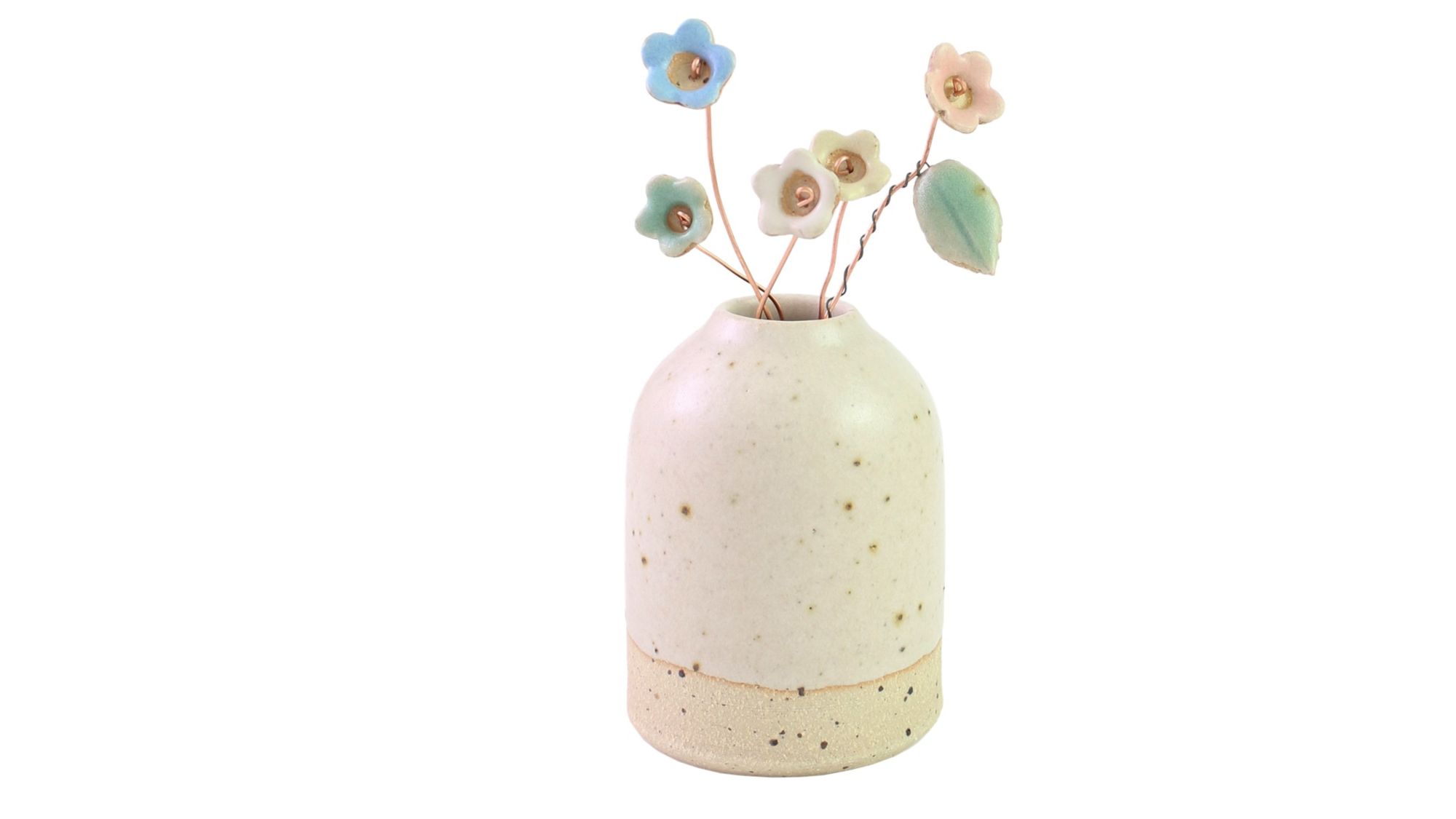 A small, cream-colored ceramic vase with speckled detailing, holding several delicate, pastel-coloured ceramic wildflower stems. The flowers are in shades of blue, pink, and yellow, and are attached to thin, brown wire stems. One stem also features a small, green ceramic leaf.