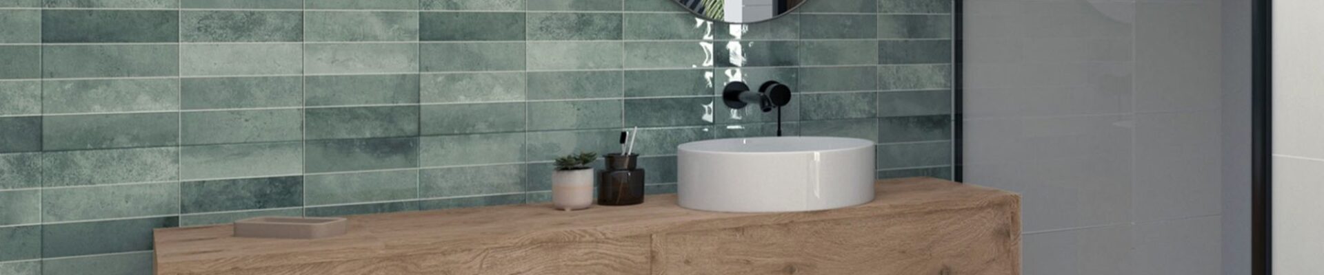 A modern bathroom interior with a focus on a stylish wall tiles. The dominant feature is the wall covered in rectangular tiles with a muted green hue. The tiles have a slightly distressed or textured appearance, adding depth and character.