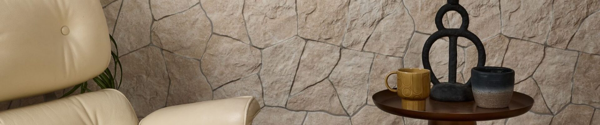 A modern living room corner featuring a cream-coloured leather armchair with a matching ottoman, positioned in front of a textured stone wall