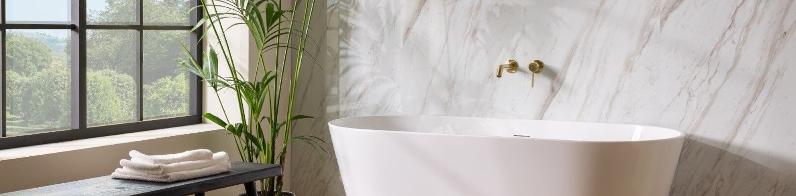 : A bright and airy bathroom featuring a freestanding white oval bathtub positioned in front of a wall with a light marble pattern.