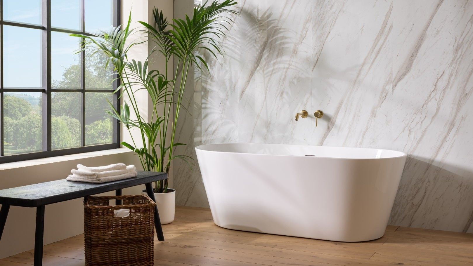 : A bright and airy bathroom featuring a freestanding white oval bathtub positioned in front of a wall with a light marble pattern.