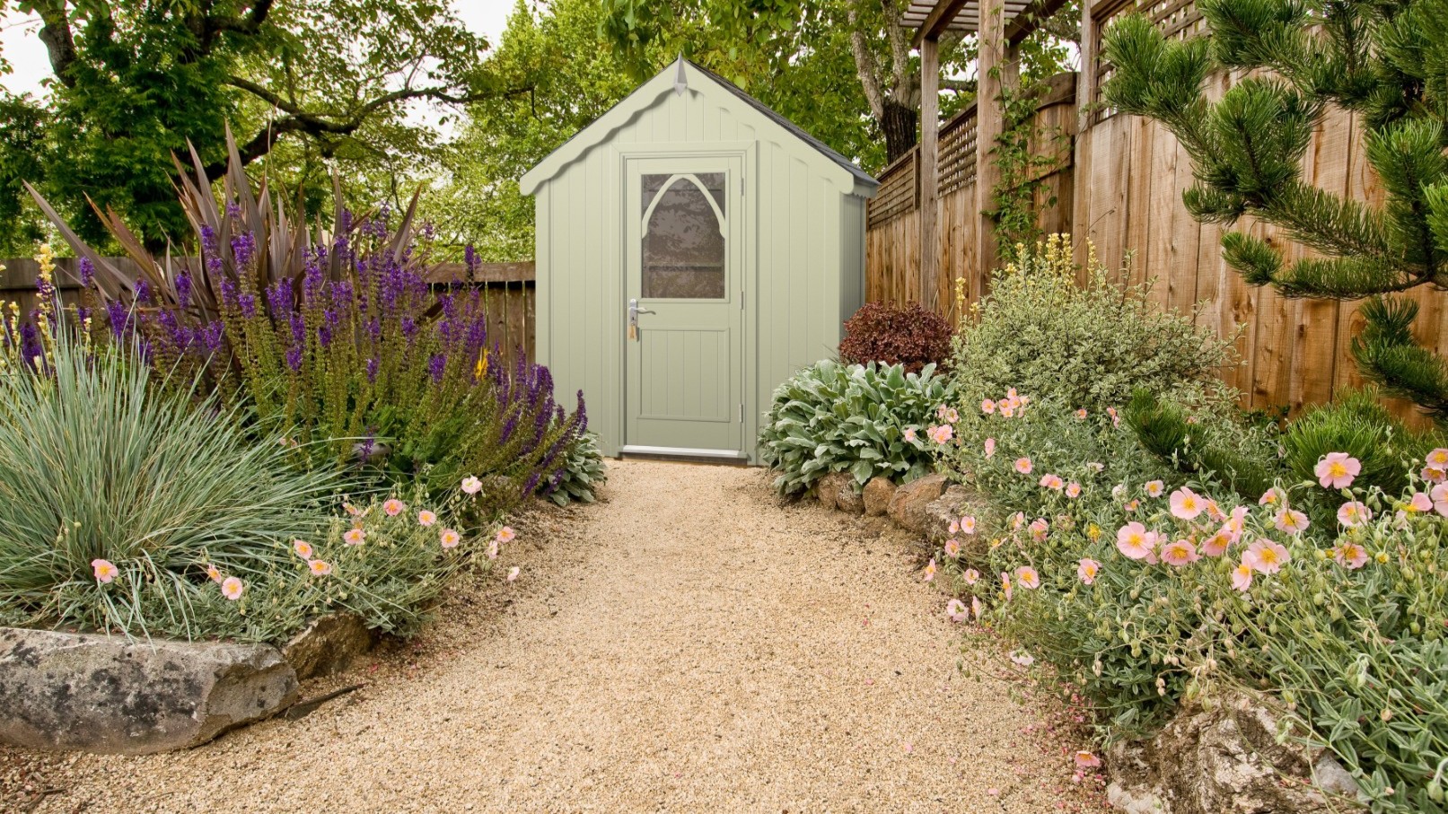 A light green wooden shed with a peaked roof and a white, arched windowed door at the far end.