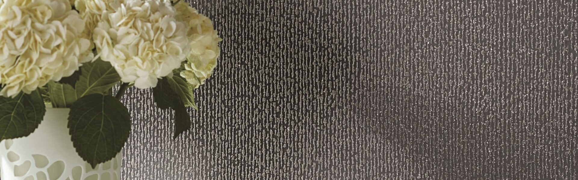 : White hydrangeas set against a textured, dark grey or charcoal-coloured wallpaper. The wallpaper has a subtle vertical pattern with a slightly speckled or granular texture