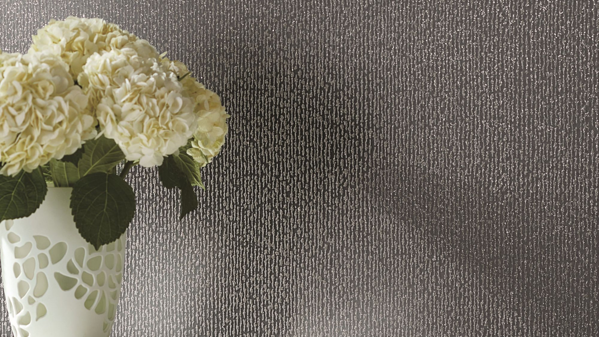 : White hydrangeas set against a textured, dark grey or charcoal-coloured wallpaper. The wallpaper has a subtle vertical pattern with a slightly speckled or granular texture