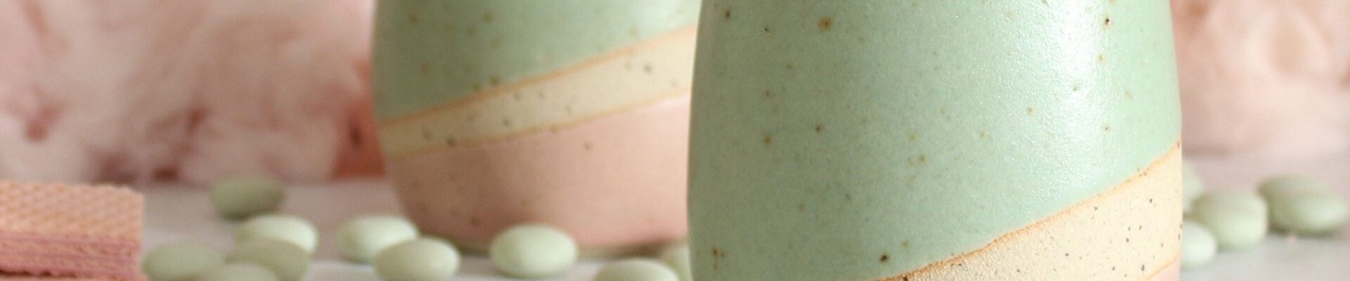 Two pastel-coloured ceramic tumblers, a light mint green on top and a soft pink on the bottom, with a creamy beige stripe separating the two colours.