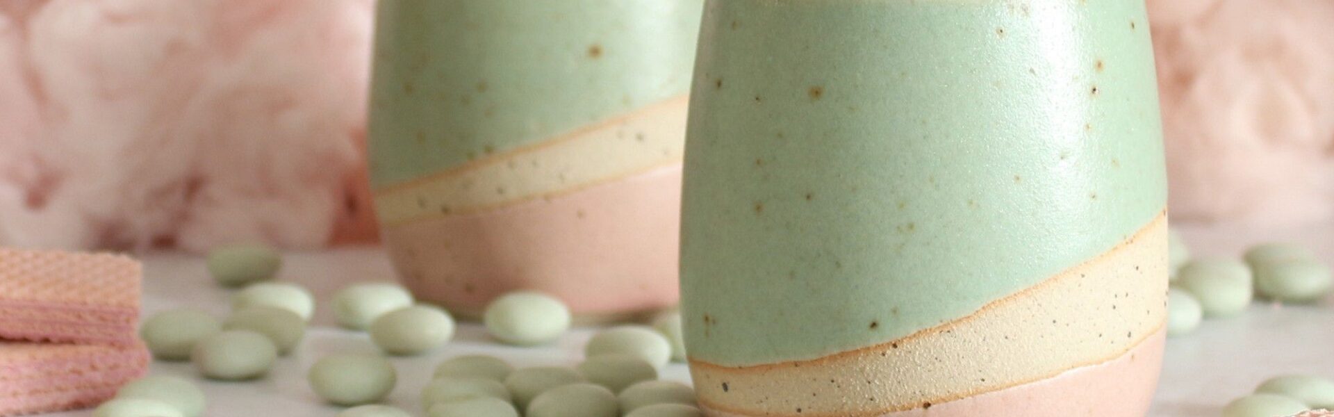 Two pastel-coloured ceramic tumblers, a light mint green on top and a soft pink on the bottom, with a creamy beige stripe separating the two colours.