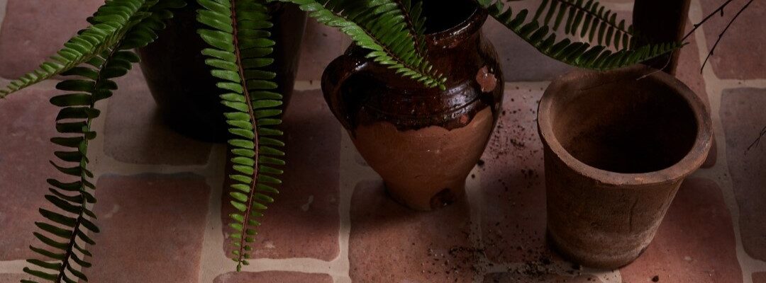 The image shows a close-up, overhead view of a rustic-looking floor made of reddish-brown terracotta tiles, laid in a brick-like pattern.