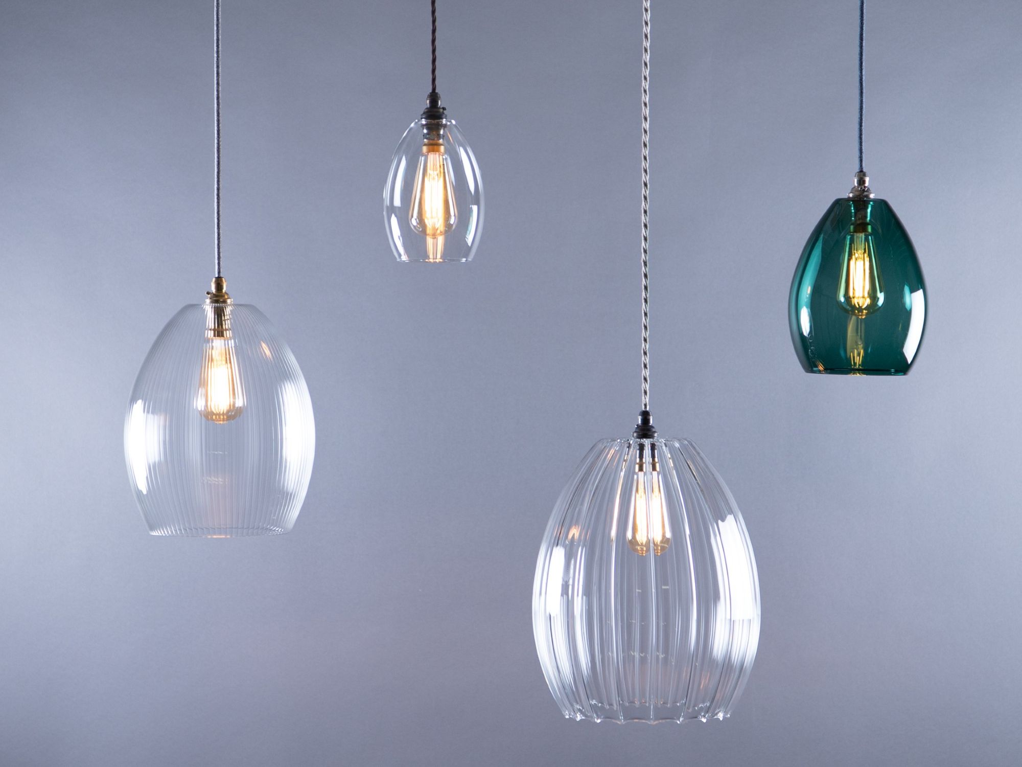 A studio shot of four pendant lights with various glass shades. All lights are hanging against a grey background.