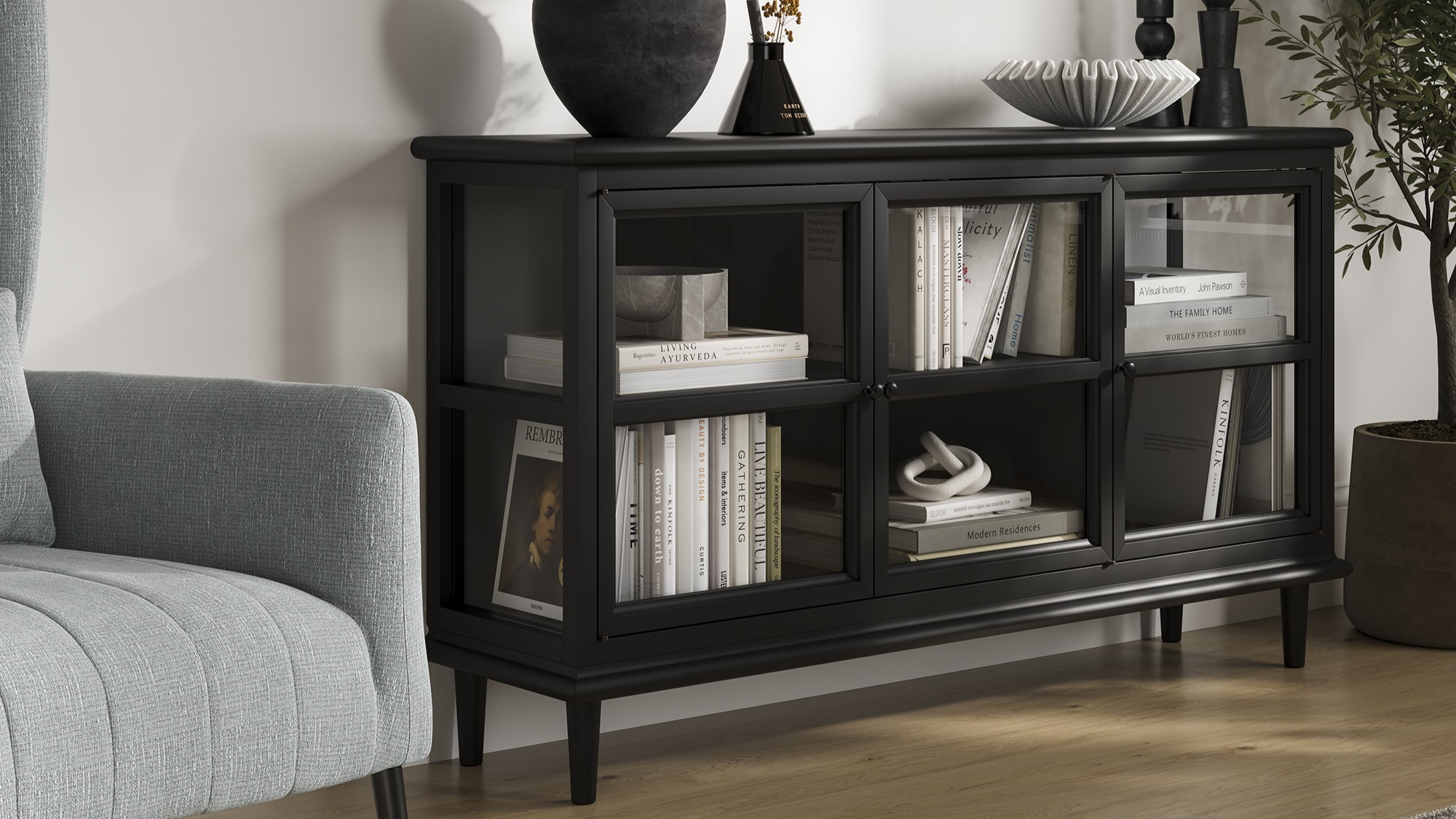 A sleek, modern black sideboard with three glass-fronted doors, each revealing two shelves filled with books and decorative objects.