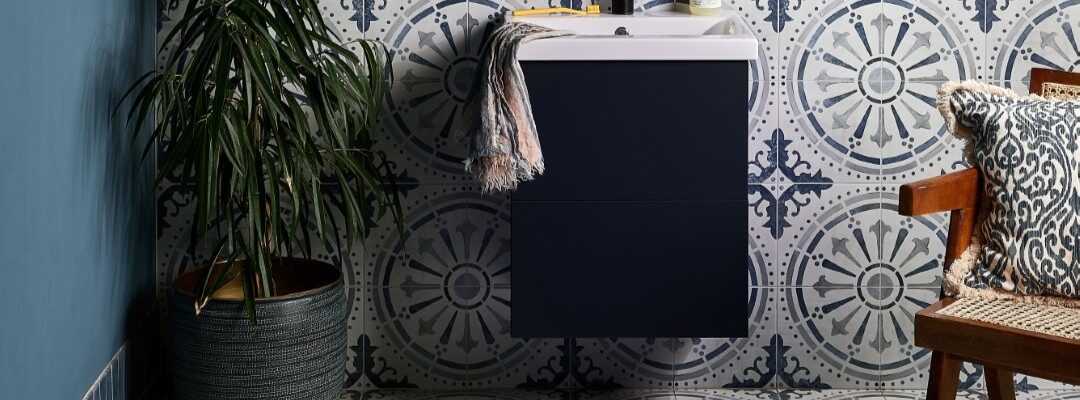 The wall features two types of tiles: a dark blue, possibly subway-style, tile on the upper part, and a patterned tile with a circular, almost mandala-like design in shades of blue and white on the lower half. This same patterned tile extends across the entire floor.
