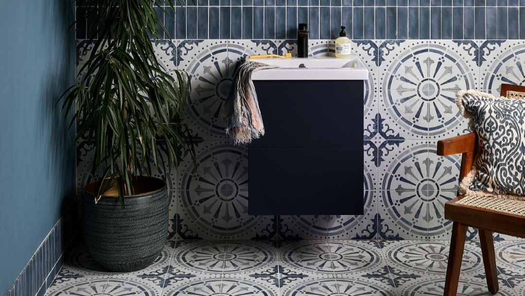 The wall features two types of tiles: a dark blue, possibly subway-style, tile on the upper part, and a patterned tile with a circular, almost mandala-like design in shades of blue and white on the lower half. This same patterned tile extends across the entire floor.