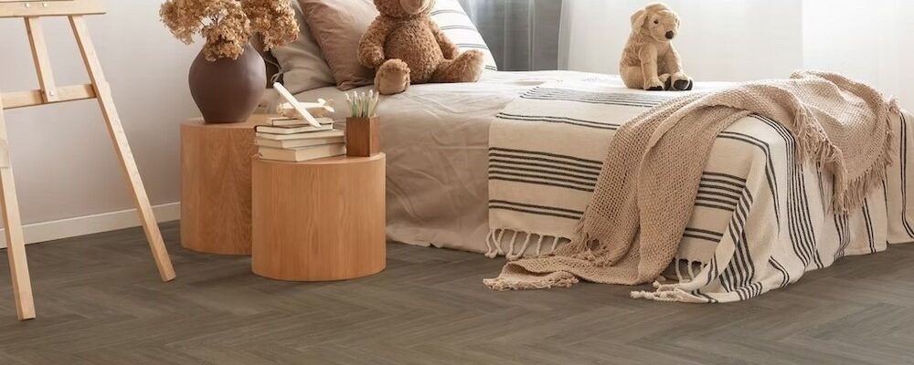 A child's bedroom with a neutral and warm aesthetic. The flooring is a dark, herringbone-patterned vinyl plank.