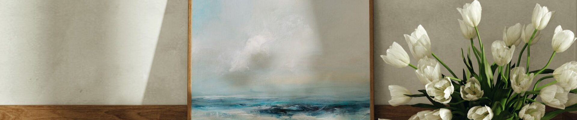 A close-up shot of an abstract painting in a thin wooden frame, standing on a rustic wooden table. The painting depicts a stormy seascape with a hazy, light-coloured sky and a dark, choppy sea with visible brushstrokes of blues and whites.