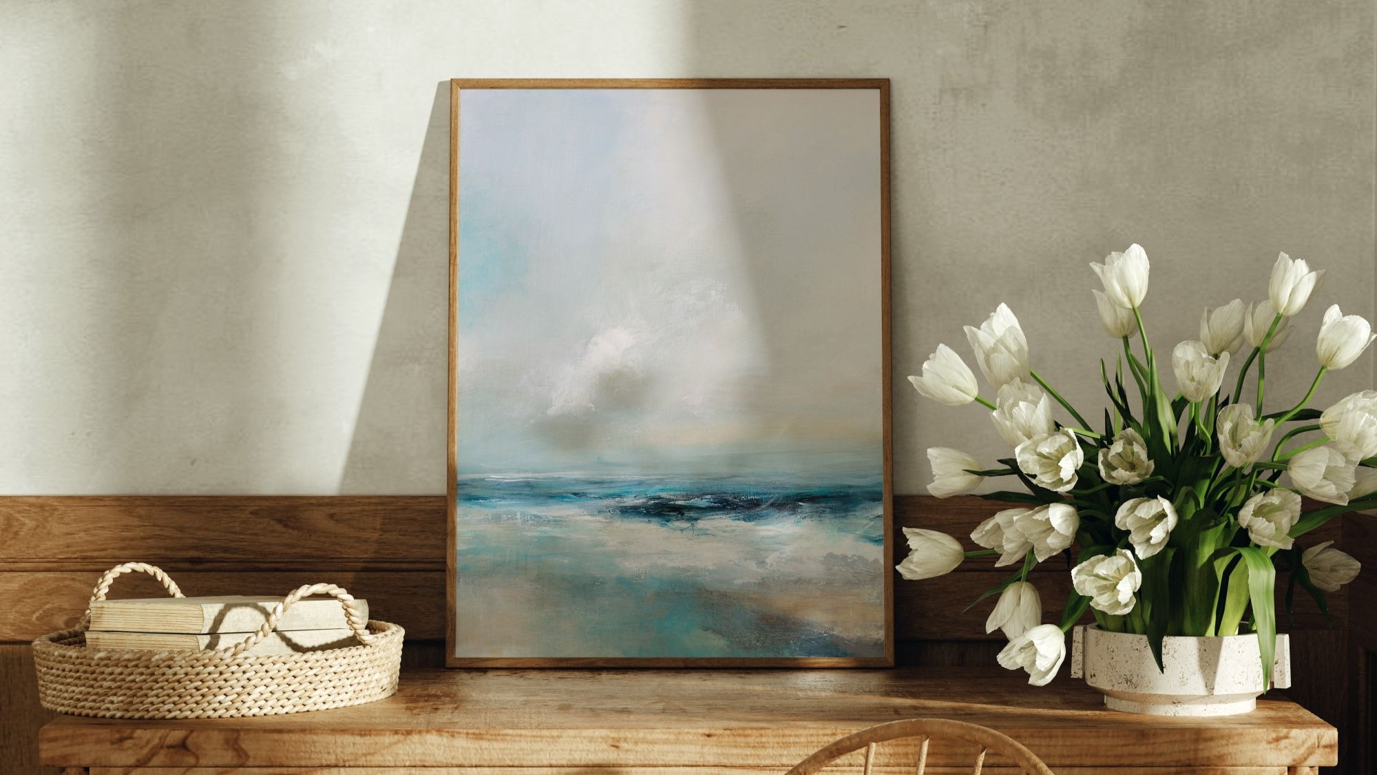 A close-up shot of an abstract painting in a thin wooden frame, standing on a rustic wooden table. The painting depicts a stormy seascape with a hazy, light-coloured sky and a dark, choppy sea with visible brushstrokes of blues and whites.