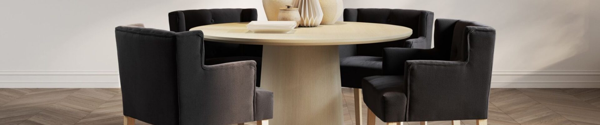 This lifestyle image showcases four Ari-Winged Dining Armchairs in anthracite, a dark gray colour, surrounding a light wood dining table. The chairs feature a clean, contemporary design with a winged backrest that curves slightly around the sides. They are upholstered in a linen blend fabric and rest on light wood legs, which complement the table.
