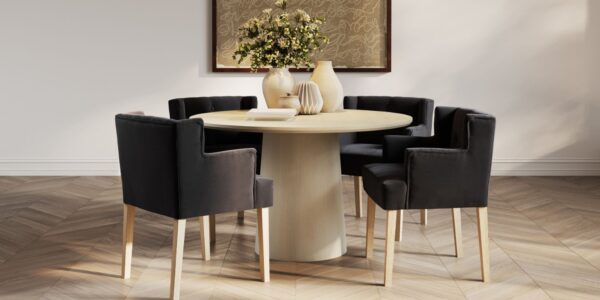 This lifestyle image showcases four Ari-Winged Dining Armchairs in anthracite, a dark gray colour, surrounding a light wood dining table. The chairs feature a clean, contemporary design with a winged backrest that curves slightly around the sides. They are upholstered in a linen blend fabric and rest on light wood legs, which complement the table.