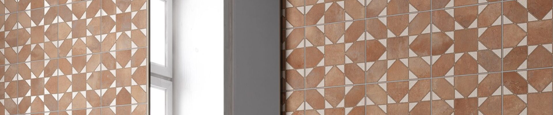 The tiles are brown with a lighter, off-white pattern. When laid out together, the pattern creates a repeating design that looks a bit like a four-petal flower or a pinwheel. The surface has a slightly textured look, almost like terracotta or clay. The grout lines are light-coloured and thin, which helps the pattern stand out.