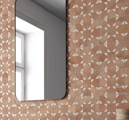 The tiles are brown with a lighter, off-white pattern. When laid out together, the pattern creates a repeating design that looks a bit like a four-petal flower or a pinwheel. The surface has a slightly textured look, almost like terracotta or clay. The grout lines are light-coloured and thin, which helps the pattern stand out.