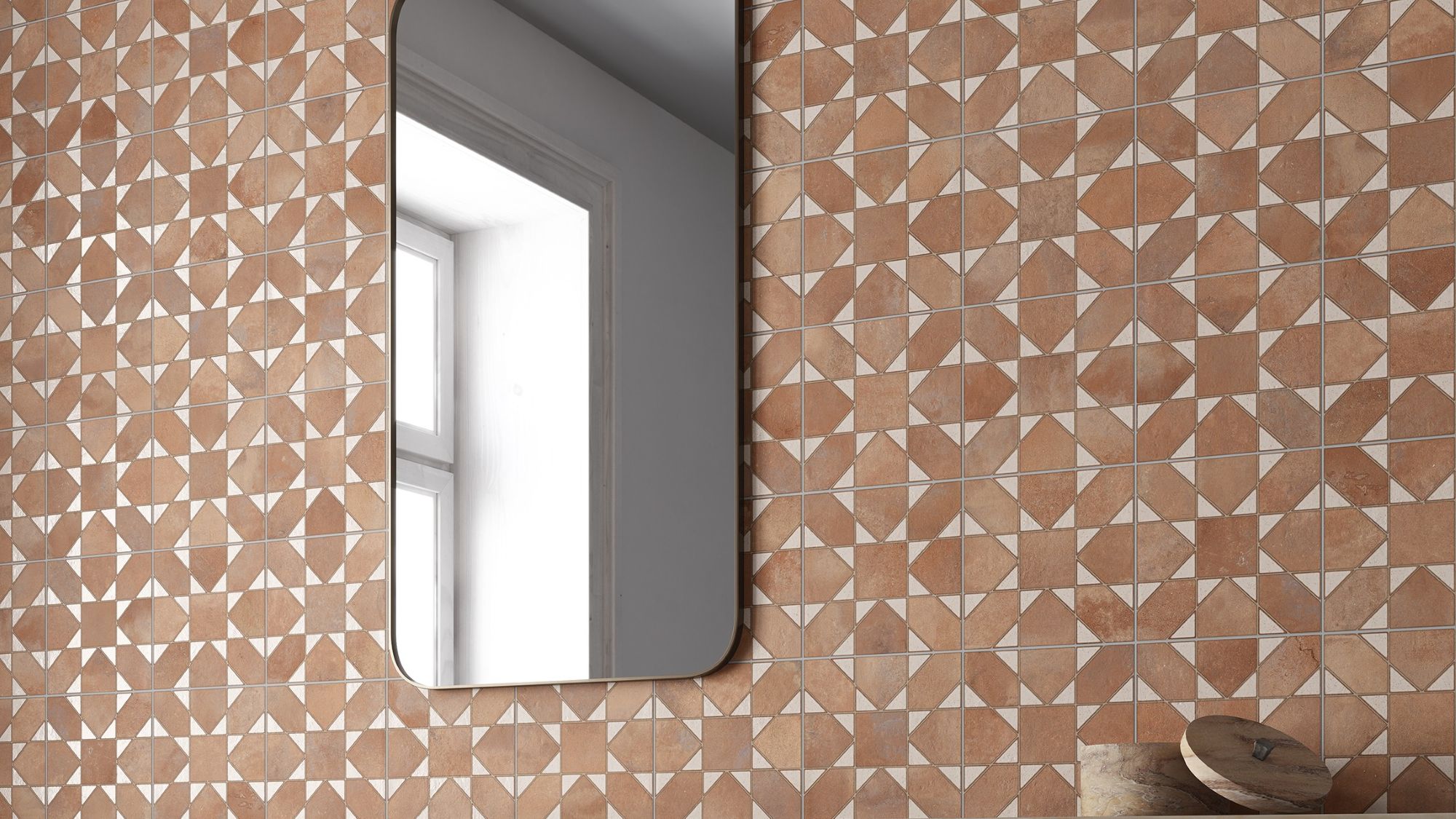 The tiles are brown with a lighter, off-white pattern. When laid out together, the pattern creates a repeating design that looks a bit like a four-petal flower or a pinwheel. The surface has a slightly textured look, almost like terracotta or clay. The grout lines are light-coloured and thin, which helps the pattern stand out.